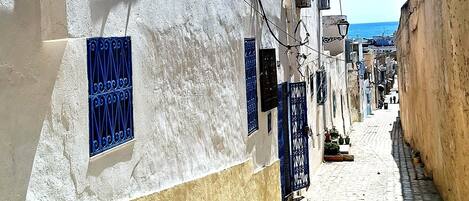 Una calle estrecha con edificios blancos, marcos de ventanas azules y un cielo azul despejado.