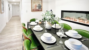 Comedor con una mesa larga dispuesta para cuatro personas, sillas verdes, platos blancos y un jarrón con flores.
