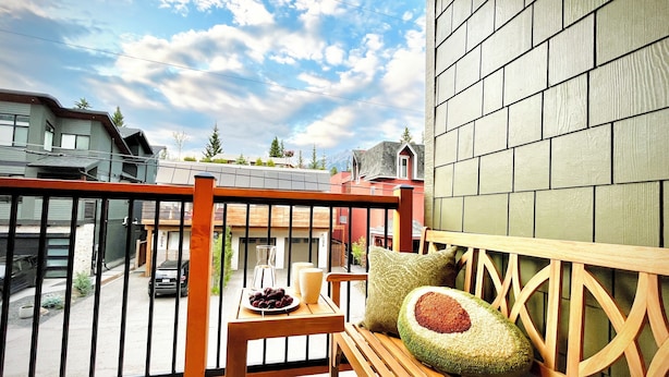 Un balcón con un banco de madera, una mesa pequeña con una fuente de fruta y un cojín.