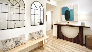 Un interior moderno con un banco de madera, dos espejos arqueados, una consola con un jarrón y un cuadro.