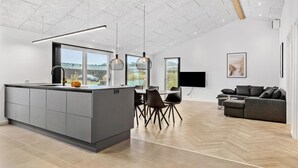 Una cocina moderna con una isla central, comedor con sillas, un sofá y un televisor montado en la pared.