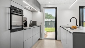 Una cocina moderna con armarios grises, horno empotrado y un ventanal con vistas al exterior.