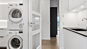 Cocina moderna con lavadoras Bosch, encimera negra y vista a un pasillo oscuro.