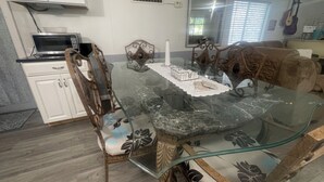 Zona pranzo con tavolo in vetro, sedie decorate, un armadietto bianco e un forno a microonde.