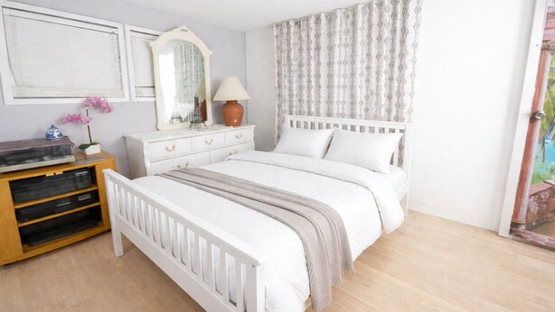 Una camera da letto con un letto bianco, una cassettiera in legno e uno specchio.