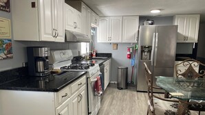 Cucina con mobili bianchi, piano cottura, macchina da caffè, cestino e frigorifero.