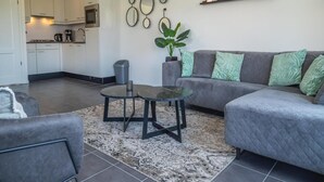 Ein modernes Wohnzimmer mit einem grauen Sofa, einem runden Couchtisch und einer Topfpflanze.