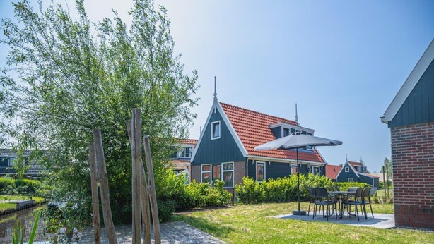 Ein Wohngebiet mit einem Haus, einer Holzterrasse, einem kleinen Teich und einer Terrasse mit Gartenmöbeln.