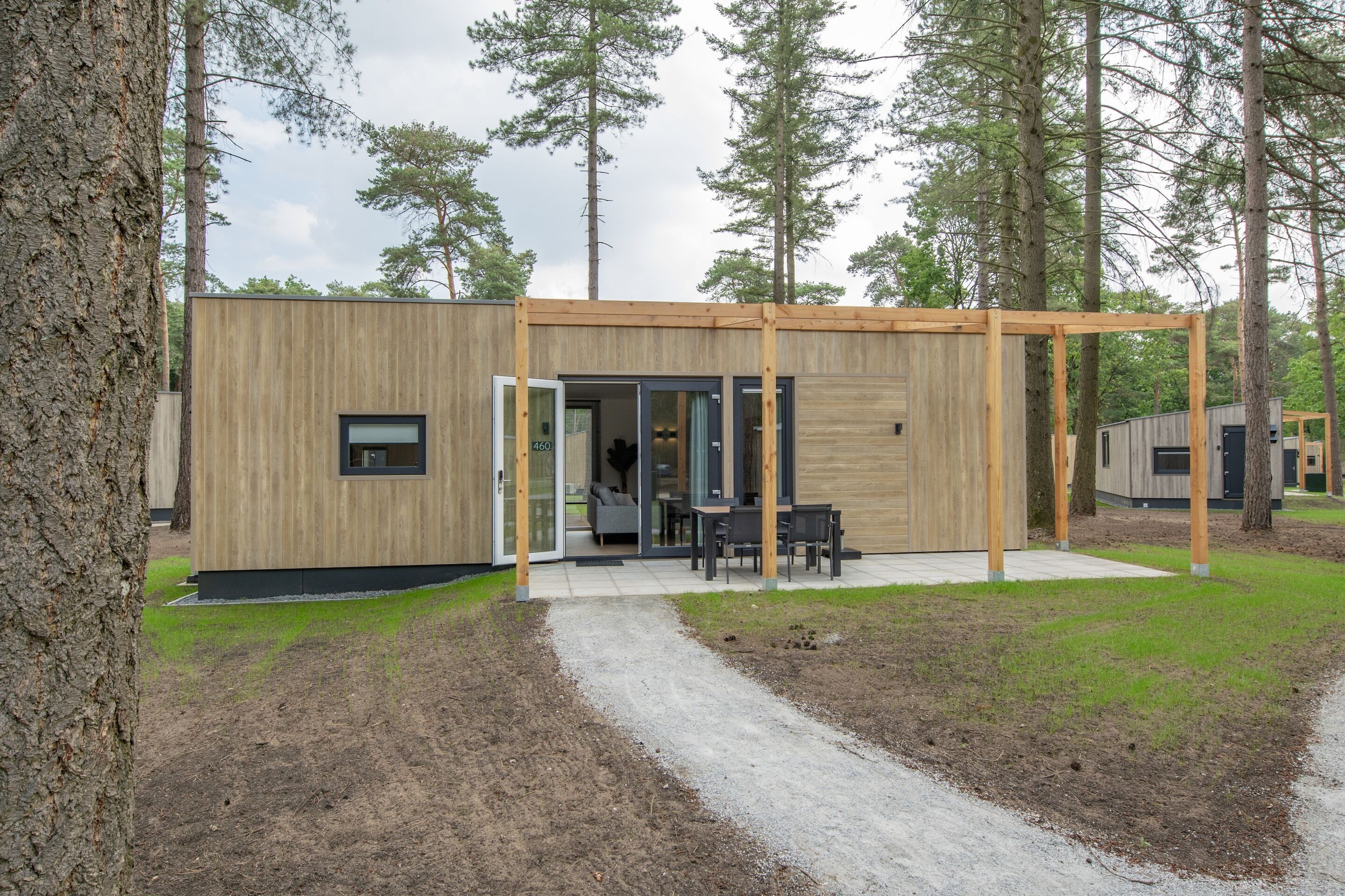 A modern wooden cabin with a covered patio, a dining area, and a visible interior with a sofa and table.