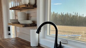 Una cocina con un grifo negro, estantes de madera y una ventana con vista a un campo.