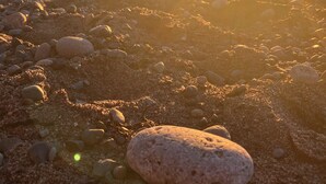 Escena de playa con piedras y una roca grande al frente.