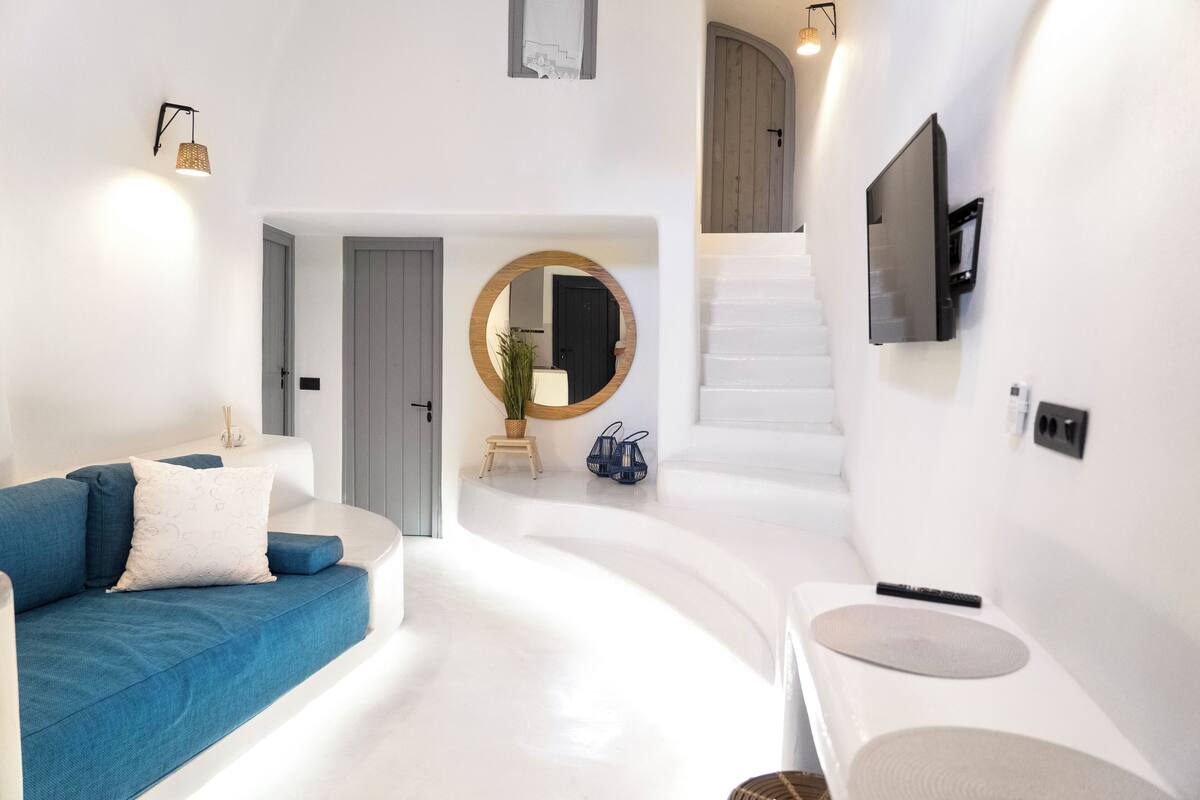 A modern living room with a blue sofa, a round mirror, and a staircase leading to an upper level.