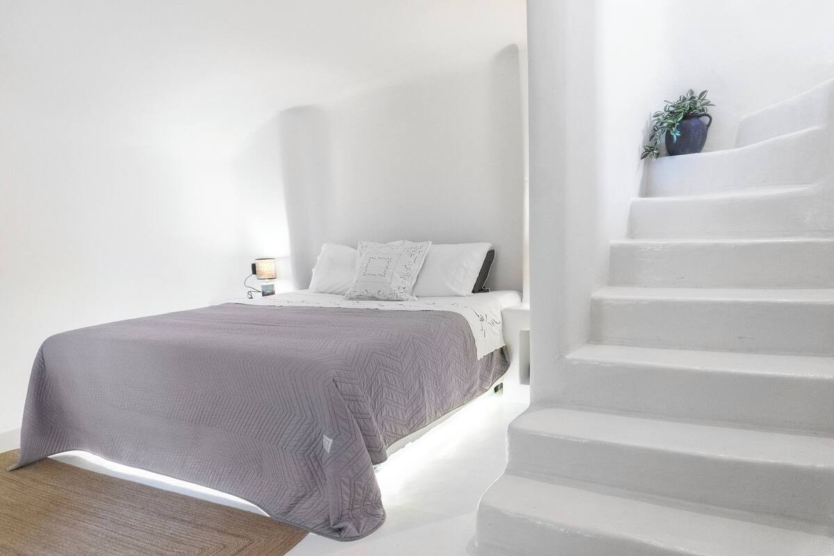 A bedroom with a bed, a bedside table, a lamp, and a staircase.