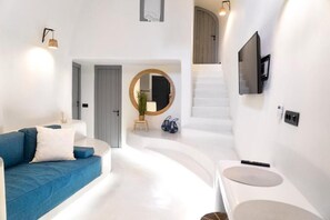 A modern living room with a blue sofa, a round mirror, and a staircase leading to an upper level. - Art and Sky (Santorini)