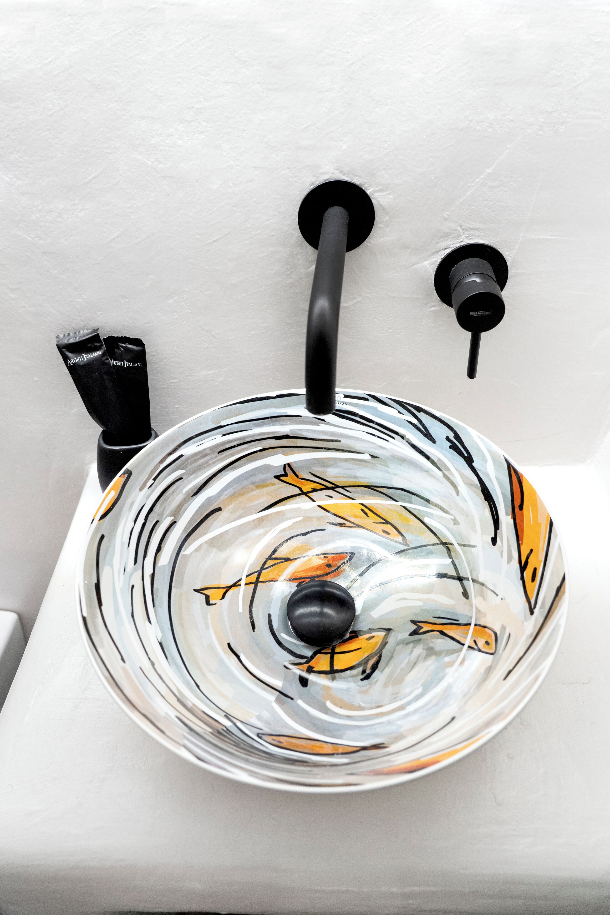 A bathroom sink with a glass bowl design, a black faucet, and a soap dispenser.