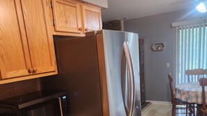 A kitchen with wooden cabinets, a stainless steel refrigerator, a microwave, and a dining area with a table and chairs.