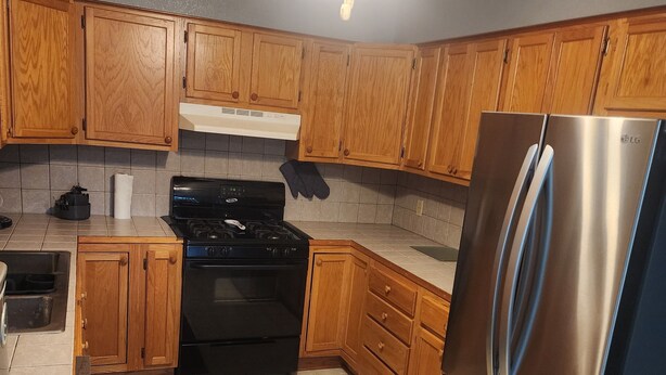 A kitchen with wooden cabinets, a stainless steel refrigerator, a black stove, and a ceiling fan.
