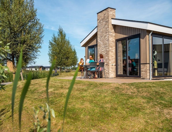 A modern building with large glass windows, a brick chimney, and a patio area with outdoor seating.