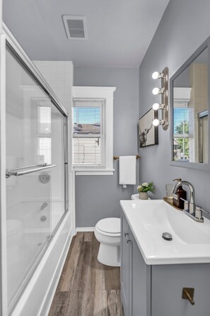 A modern bathroom with a glass shower enclosure, a white toilet, and a vanity with a sink and mirror.