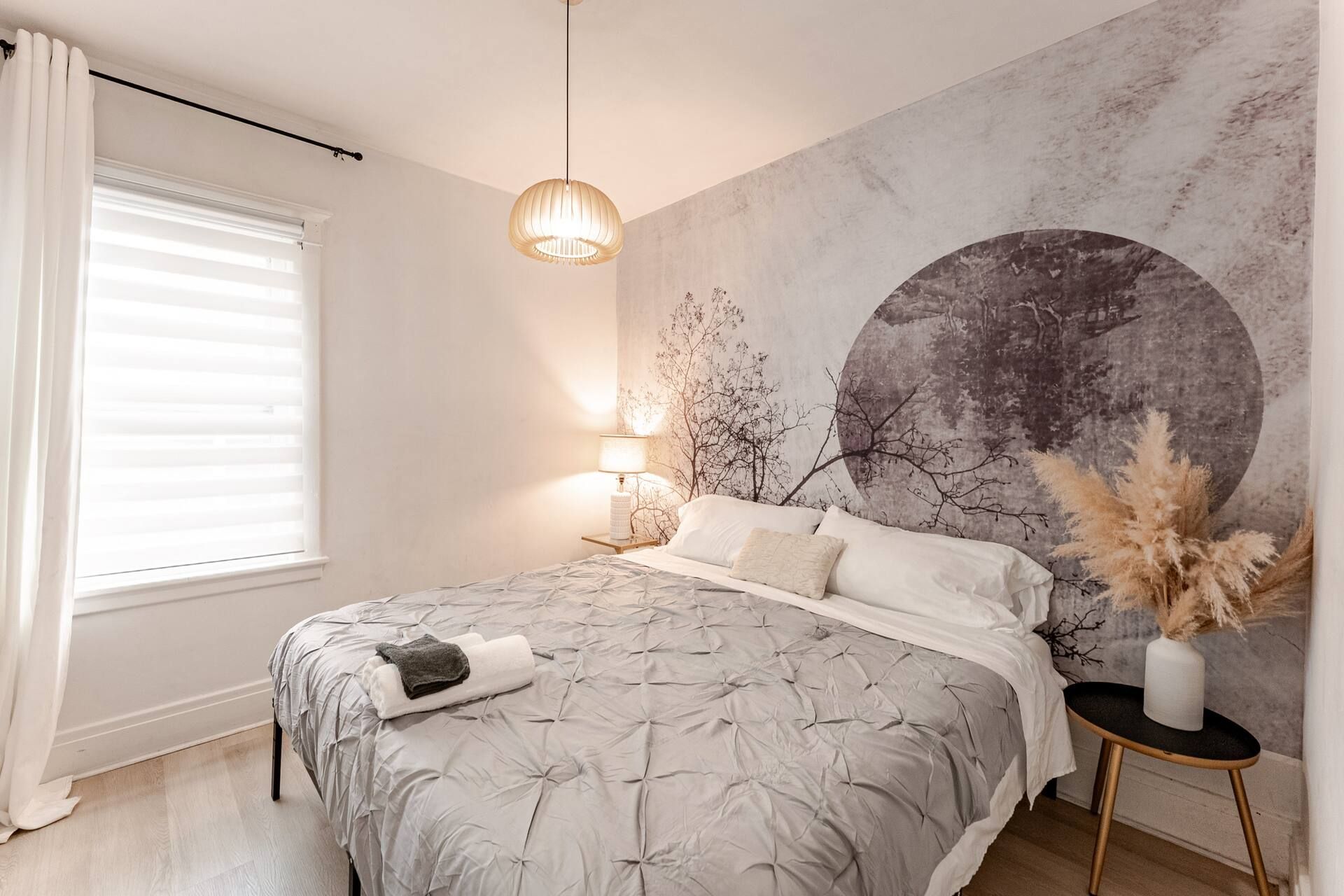 A bedroom with a bed, a wall-mounted lamp, and a window with blinds.