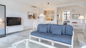 Un salon moderne avec un canapé, un téléviseur et un coin repas avec des chaises.
