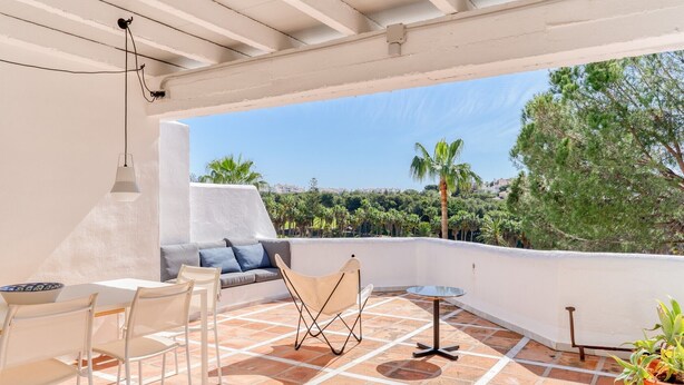 Une terrasse extérieure avec un plafond blanc, un canapé, des chaises, une petite table et une plante en pot.
