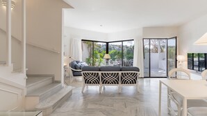 Un salon moderne avec un canapé, une table à manger et une vue sur l’extérieur, accessible par une porte vitrée.
