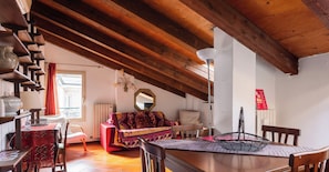 Una habitación acogedora con techo de madera, una mesa de comedor con sillas, un sofá y una pequeña mesa con lámpara.