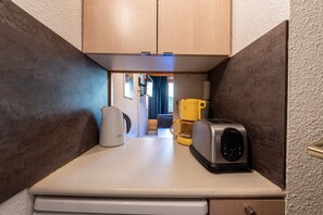 Una kitchenette compacta con cafetera, tostadora y un recipiente amarillo.