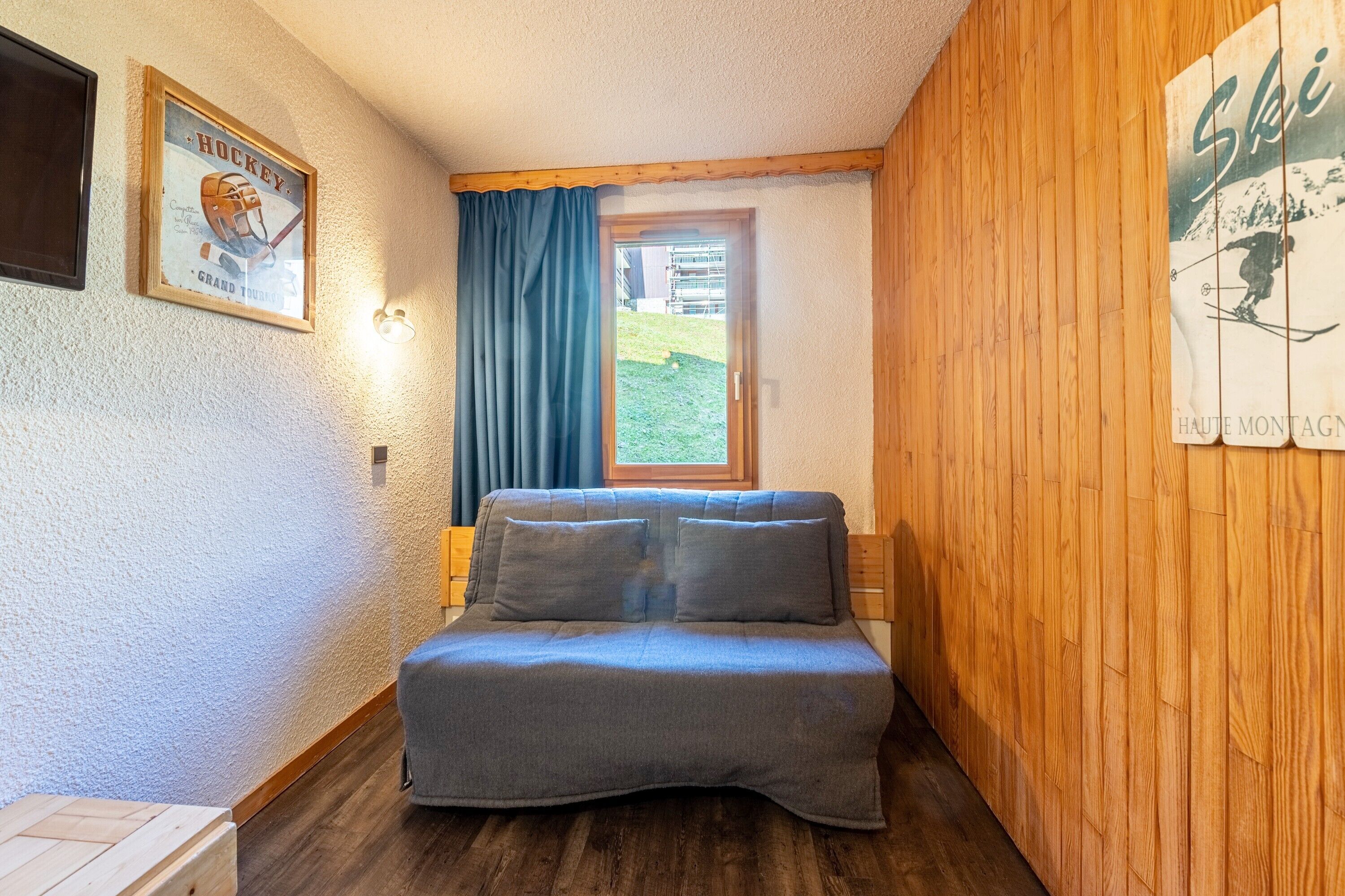 A cozy room with a bed, a window, a framed hockey poster, and a wooden wall.