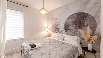 A bedroom with a bed, a wall-mounted lamp, and a window with blinds.