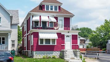 A two-story house with a red and white exterior, a balcony with a white awning, and a front porch with a bench.