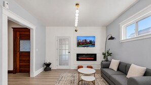 Un salon comprenant un canapé, un téléviseur, une cheminée et un coin repas avec une table et des chaises.