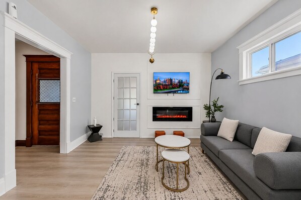 Una sala de estar con sofá, televisor, chimenea y un comedor con mesa y sillas.