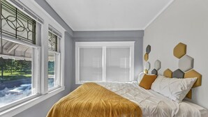 Une chambre à coucher avec un lit, une fenêtre avec des stores et une vue sur l’extérieur.