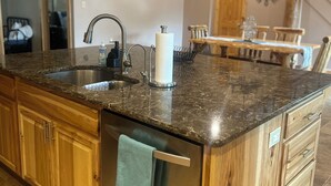 Una cocina con encimera de granito, pileta de acero inoxidable, muebles de madera e iluminación colgante.