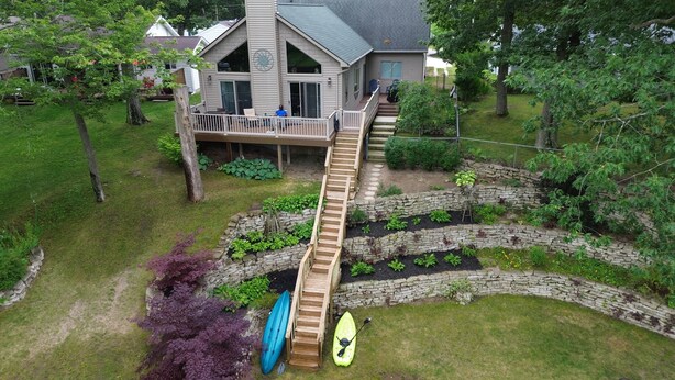 Una casa con terraza de madera, un muro de contención de piedra y un kayak.
