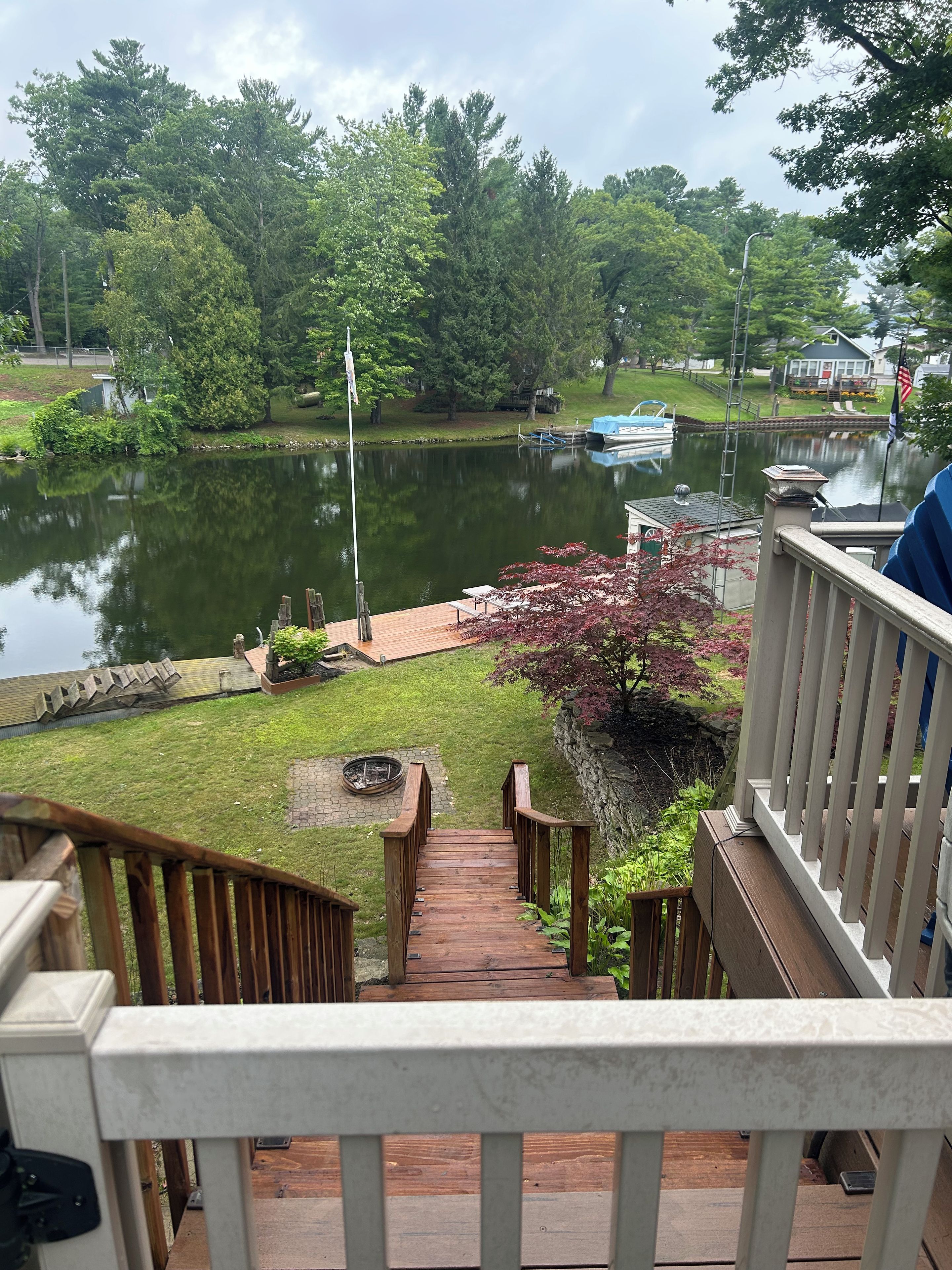 A wooden deck leading to a grassy area with a pond, dock, and boats.