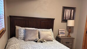 Una camera da letto con una testiera in legno, una coperta a motivi decorativi e un comodino con una lampada e una cornice con un'immagine.