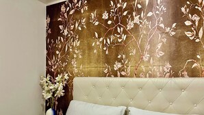 A bedroom with a tufted headboard, white bedding, and a floral wallpaper design. - Niagara RiversideView Balcony GameRoom WiFi Free Parking King bed Crib sleep 9 (Buffalo)