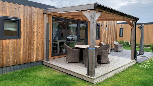 Fachada de madera con un patio cubierto que incluye mobiliario de mimbre y una puerta de vidrio.