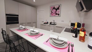 A modern kitchen with a long island, equipped with a built-in oven, microwave, and a coffee machine. There are two wine glasses and a bottle of wine on the island. - Luxury One Bedroom Apartment in Berkshire  (Reading)