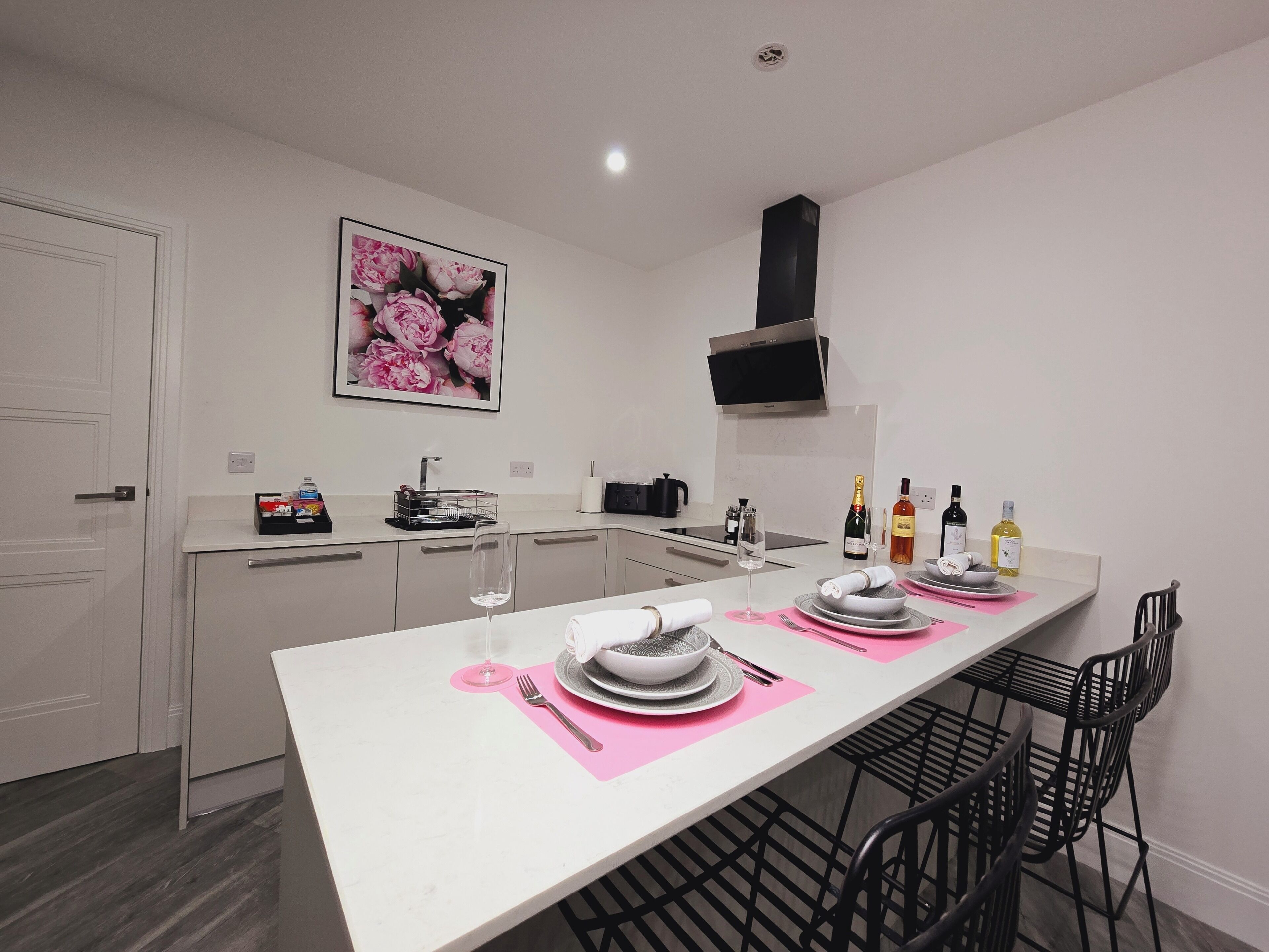 A modern kitchen with a white countertop, a dining table set with plates, glasses, and cutlery, and a black chair.