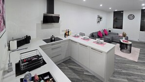 A modern kitchen with a central island, built-in appliances, and a dining area with a sofa and coffee table. - Luxury One Bedroom Apartment in Berkshire  (Reading)