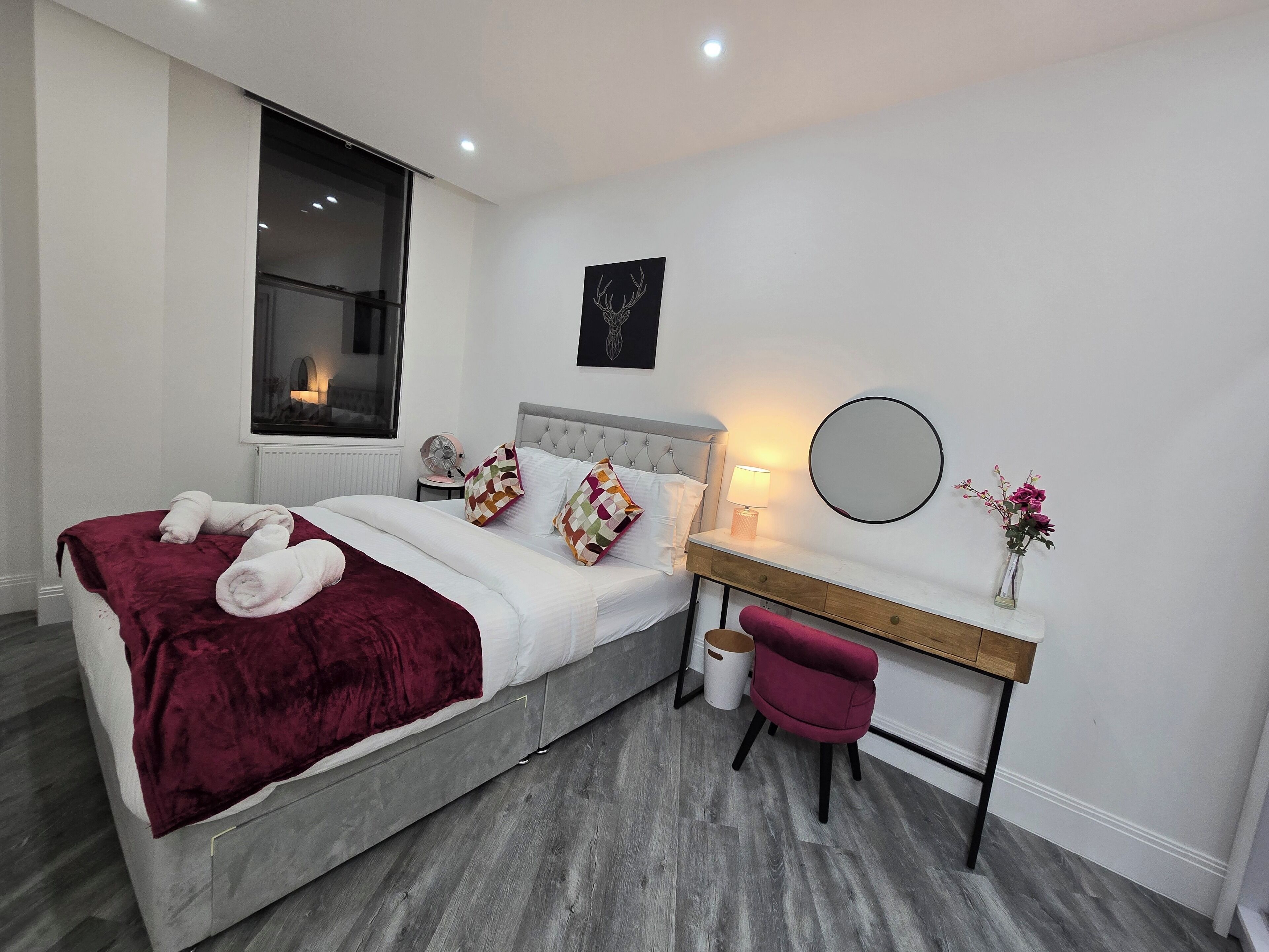 A modern bedroom with a bed, bedside table, chair, and a desk with a mirror.