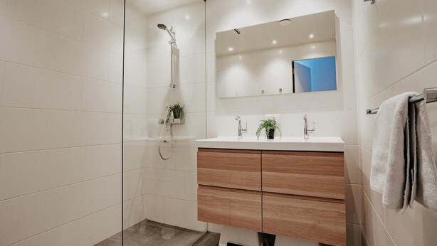 A modern bathroom with a glass shower enclosure, a white vanity with wooden drawers, and a mirror above the sink. - Waterside Escape With Easy Access (Uitgeest)