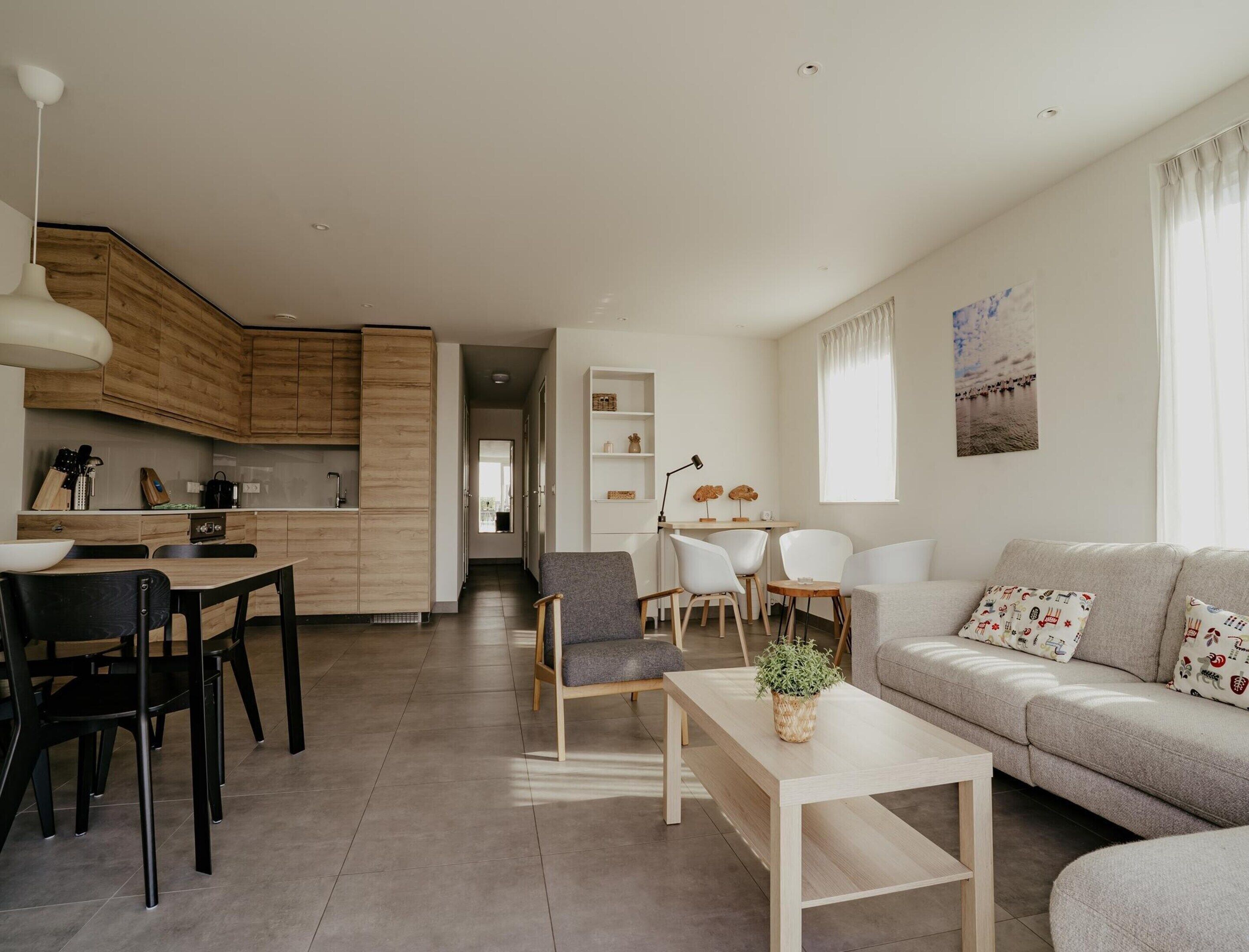 Una sala de estar moderna con un sofá gris, una mesa de centro y una zona de comedor con una mesa y sillas de madera.
