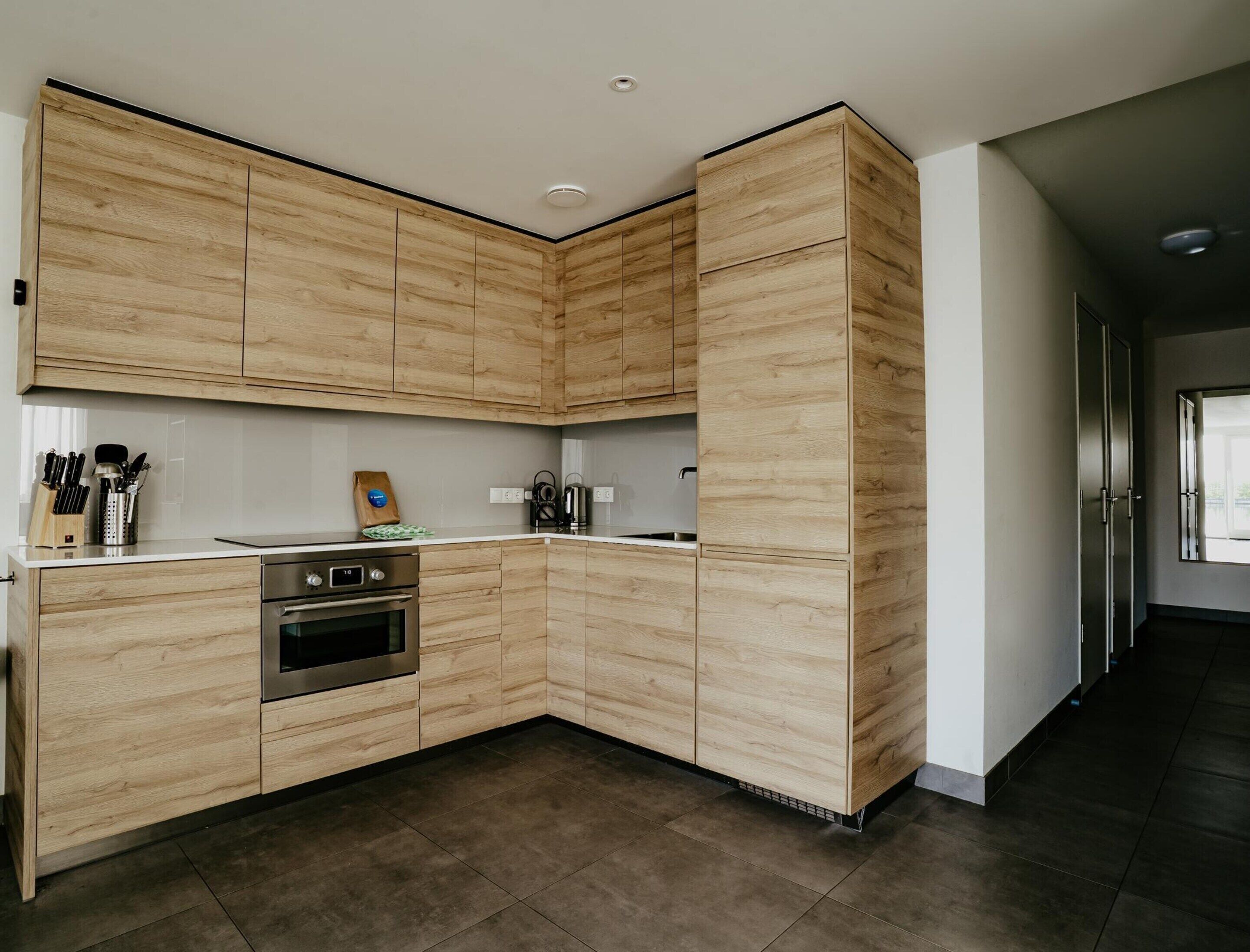 A modern kitchen with wooden cabinets, a stainless steel oven, and a countertop with kitchen utensils.