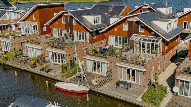 A canal-side residential area with modern houses featuring large windows, outdoor seating, and a boat docked nearby. - Waterside Escape With Easy Access (Uitgeest)