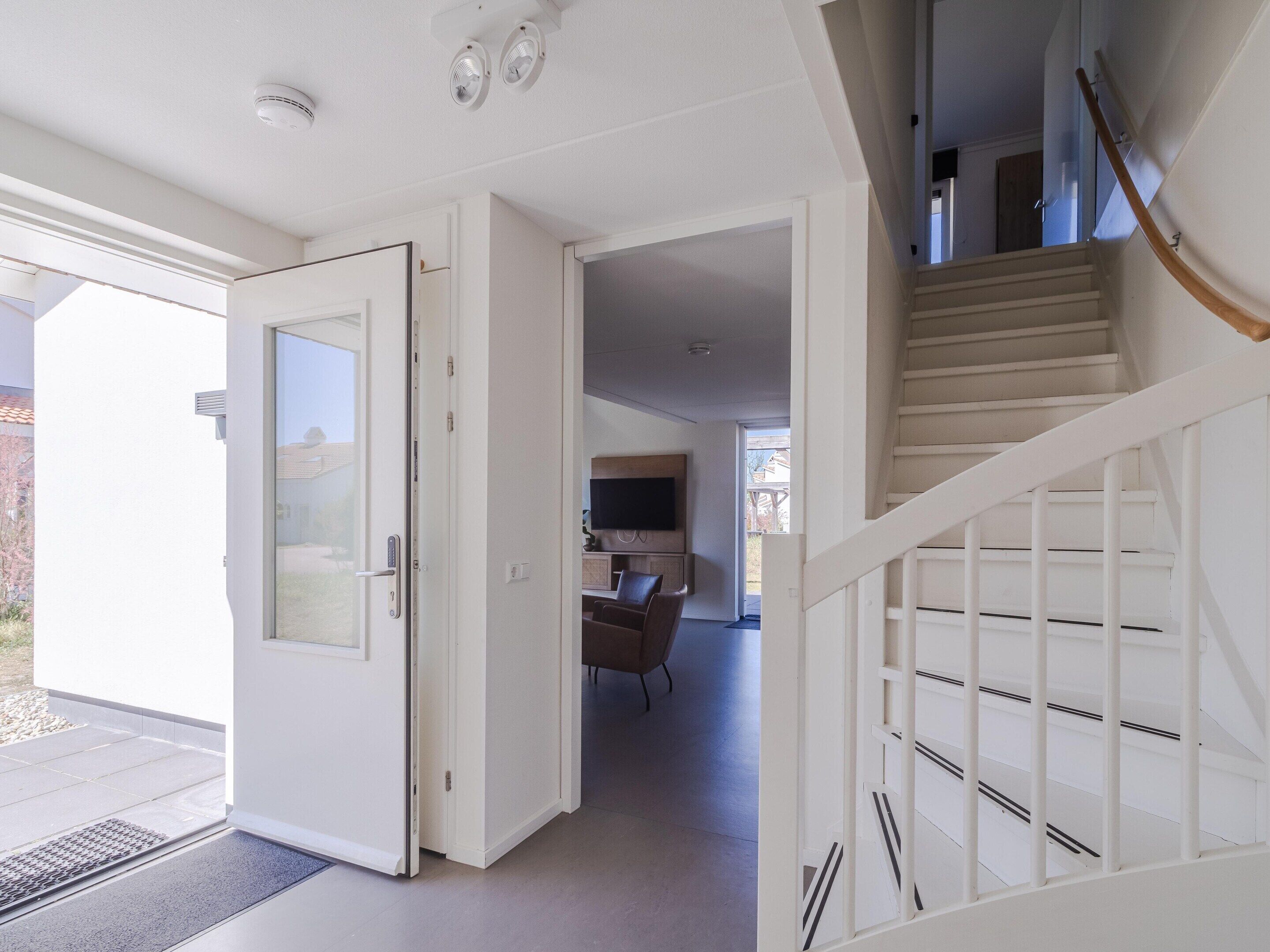 A modern interior with a staircase, a door leading to an outdoor area, and a visible kitchen area.